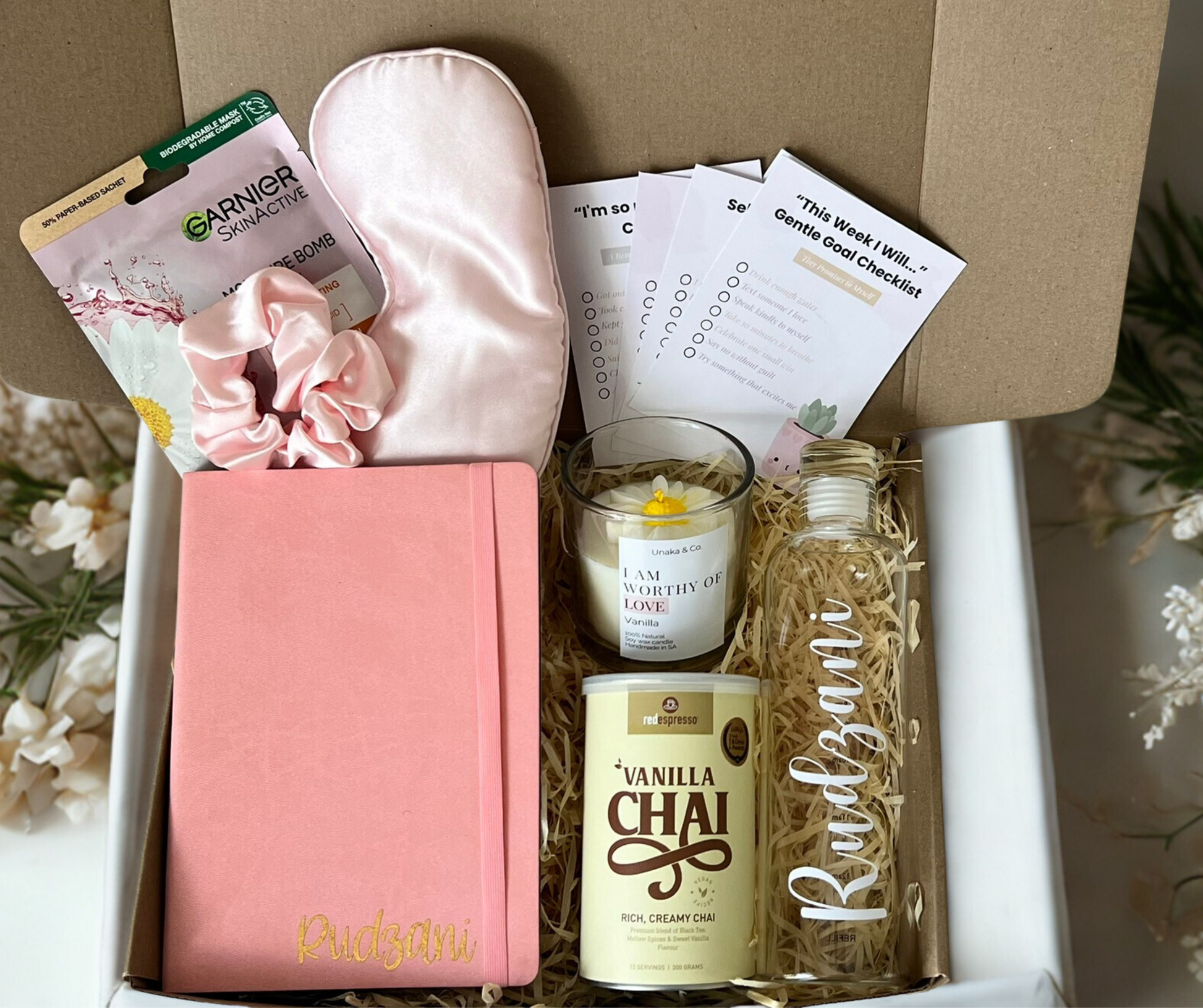 Gift box with pink notebook, candle, and other items on a neutral background